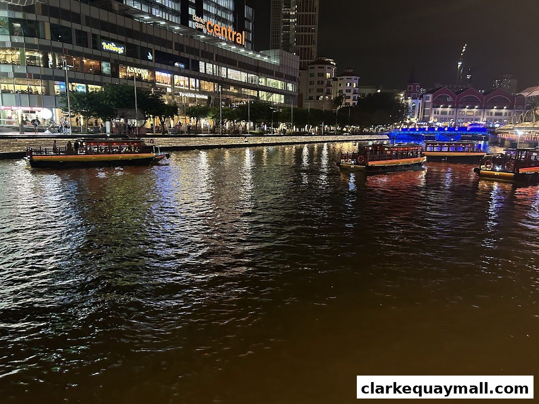 Night view of Clarke Quay with boats on the river and illuminated buildings.
