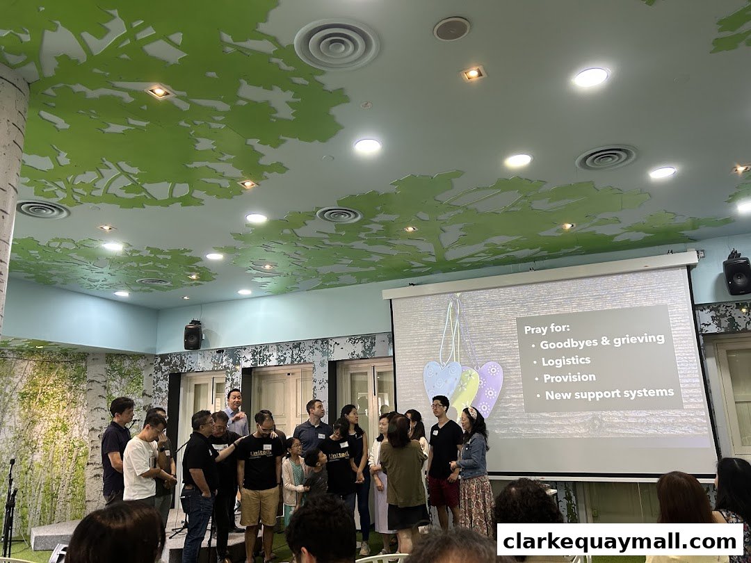 A group of people stand in front of a projector screen with a list of prayer requests.