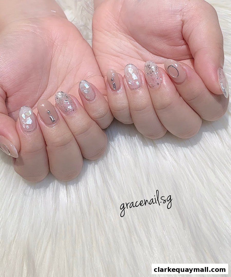 Close-up of hands with elegant, neutral-toned nails featuring glitter and shell accents.