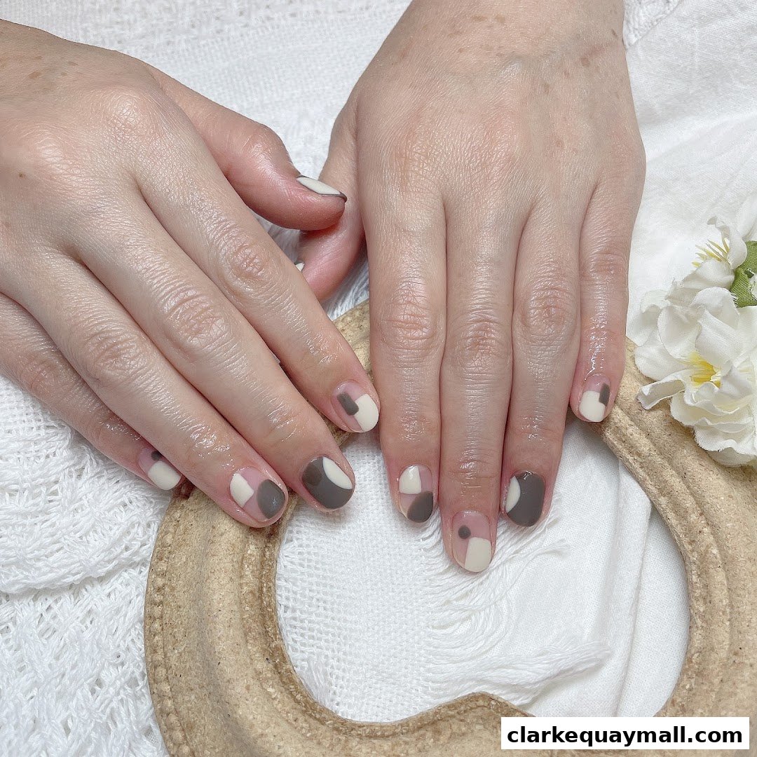 A close-up of hands with stylish geometric-patterned nails in neutral tones.