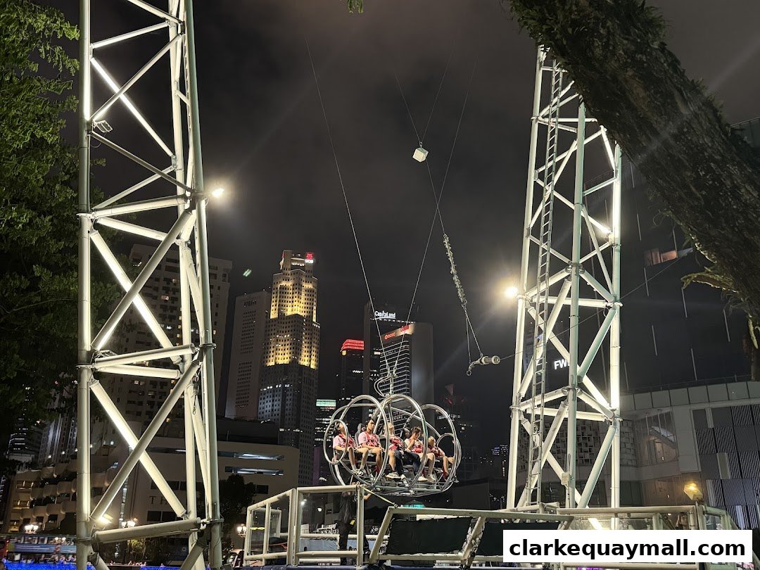 People riding the GX-5 Extreme Swing at night with city skyline in the background.