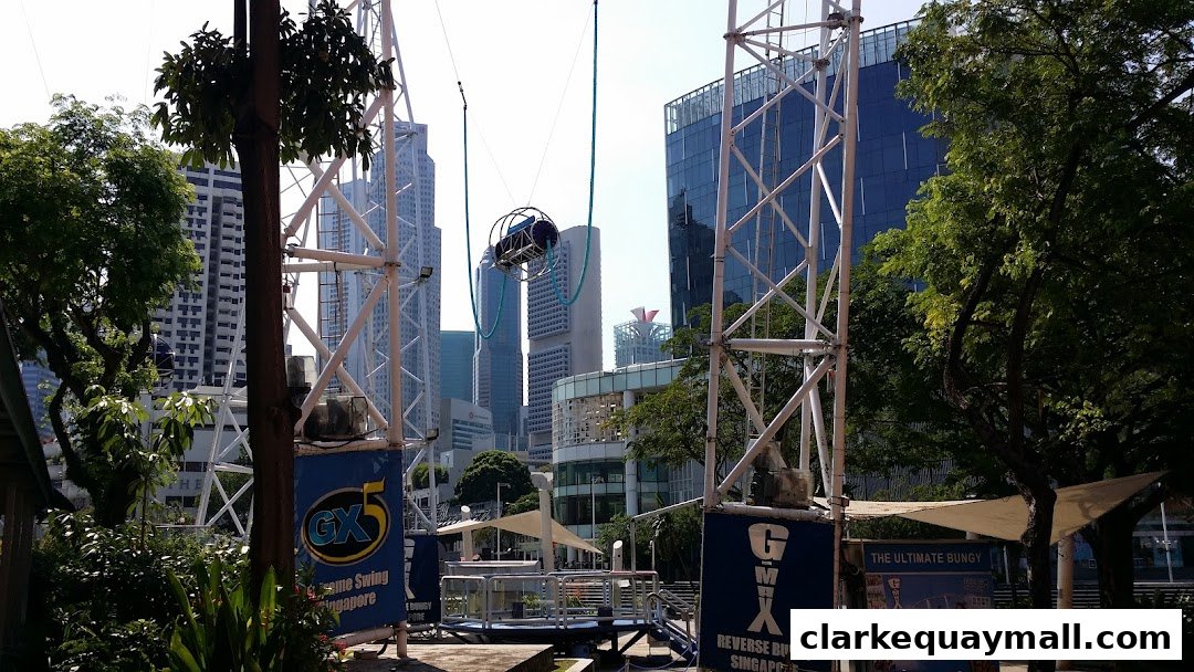 A tall swing ride structure with a basket suspended in the air against a city skyline.