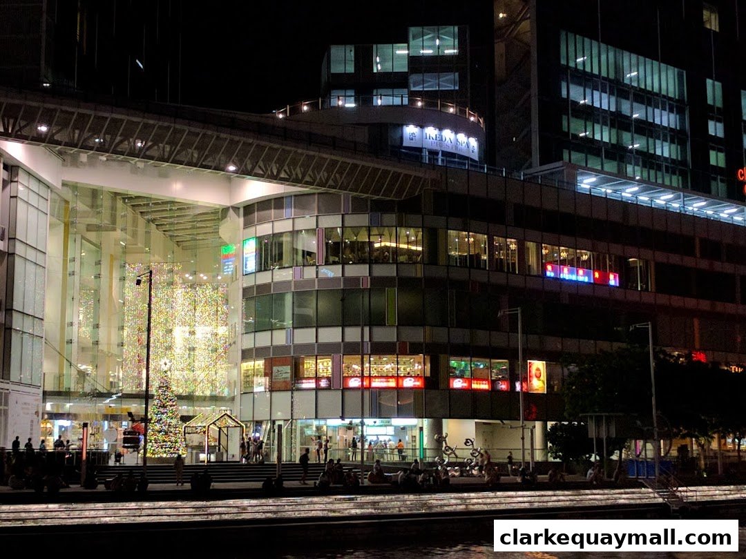 A modern shopping mall exterior at night, featuring illuminated windows and a festive Christmas tree.