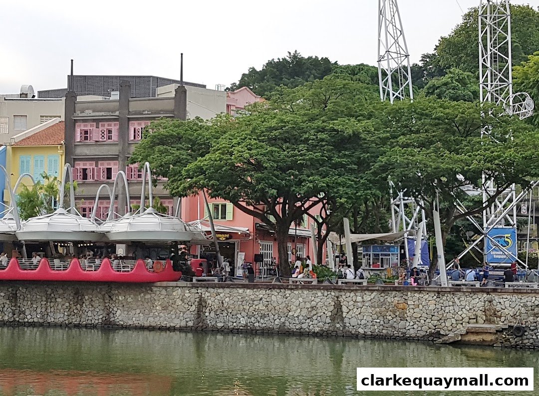 A waterfront scene with colorful buildings, trees, and a large swing ride.