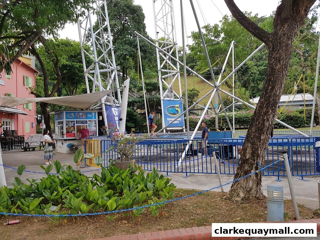 People enjoying the GX-5 Extreme Swing attraction with its tall metal structure and blue safety barriers.