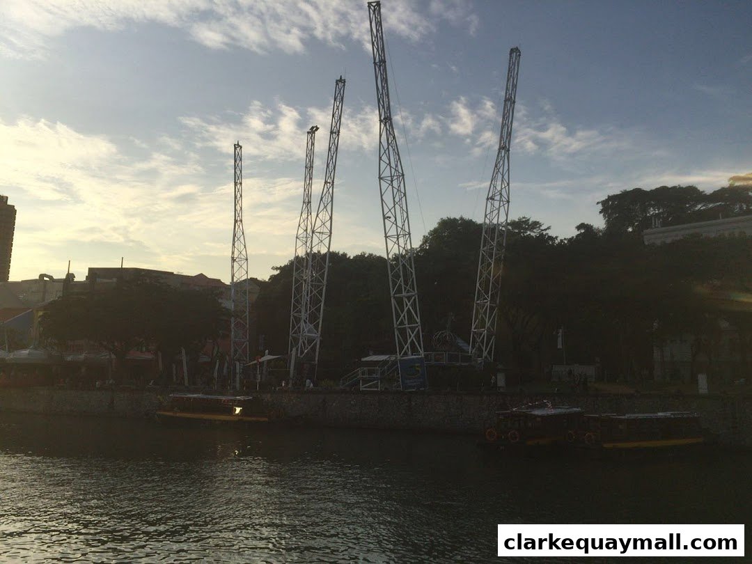 Tall swing structures stand over a river with boats docked along the bank.