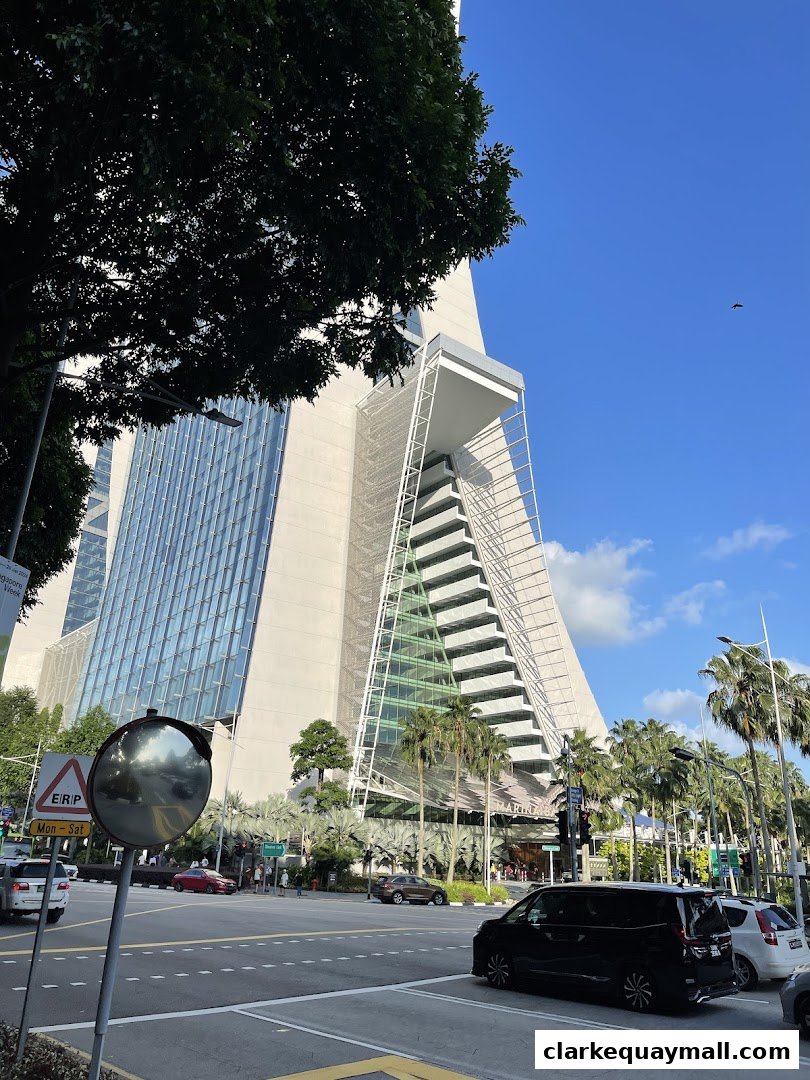 A modern skyscraper with a unique architectural design, surrounded by palm trees and a street scene.