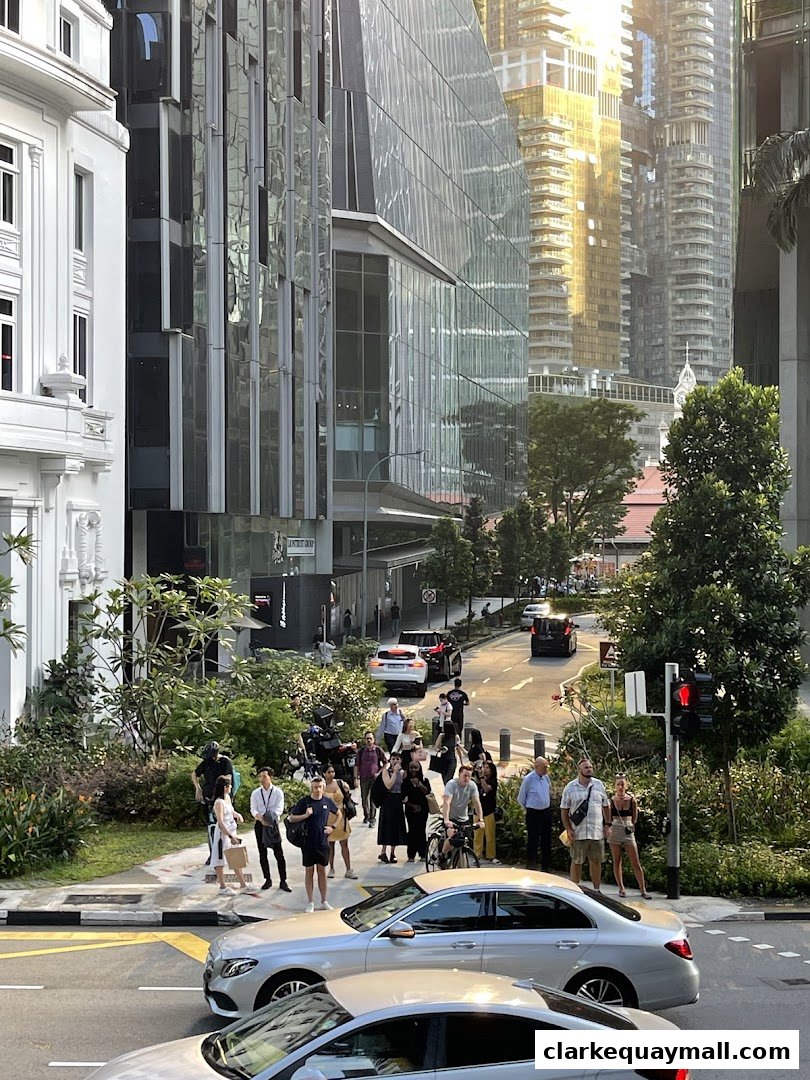 People and cars on a street with modern buildings and greenery.
