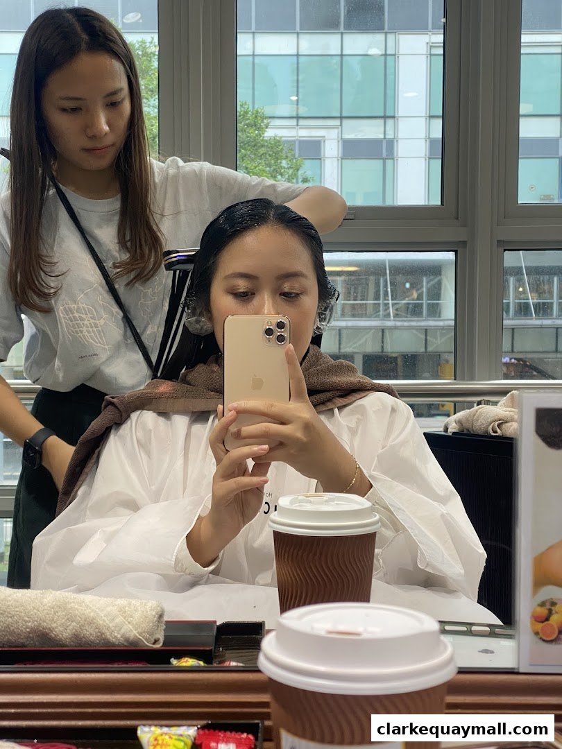A woman takes a selfie while a stylist works on her hair in a salon.