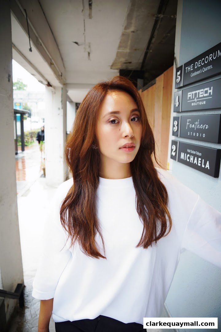A woman with long brown hair stands in front of a building with shop signs.