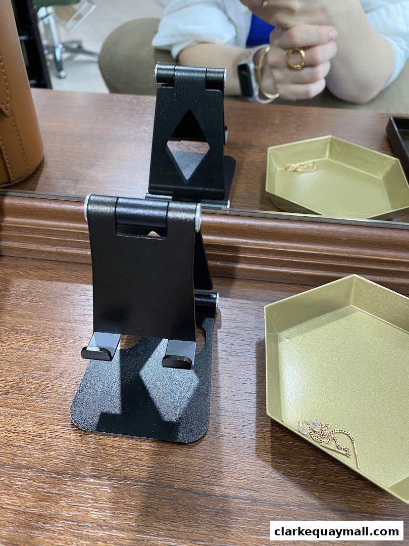 A close-up of a wooden counter with a phone stand and a jewelry tray.
