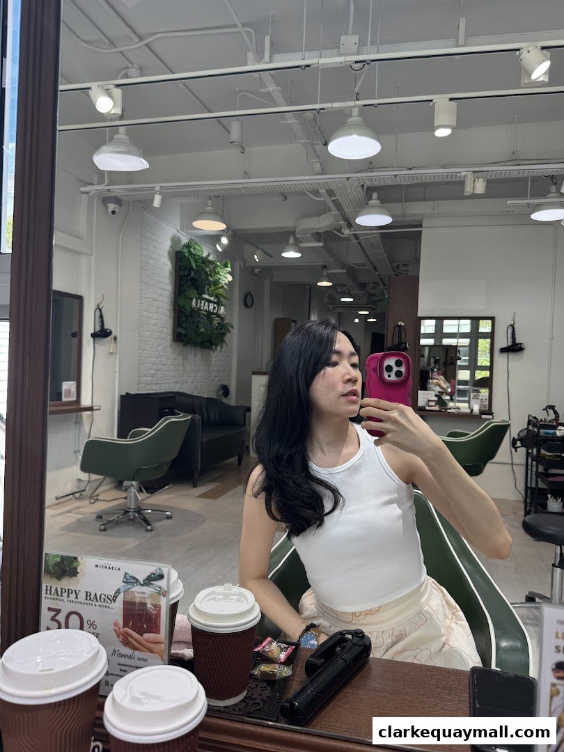 A woman takes a selfie in a salon mirror, with coffee cups and a promotional flyer visible.
