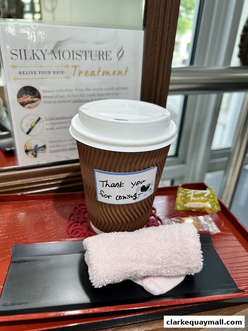 A cup of coffee with a 'Thank you for coming' note, a small towel, and a hair treatment flyer.