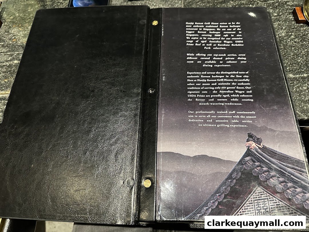 A black leather-bound menu open to a page with descriptive text about Hanjip Korean Grill House.