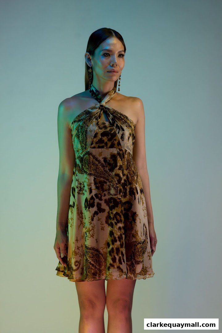 A woman models a short, patterned dress with a halter neckline and statement earrings.