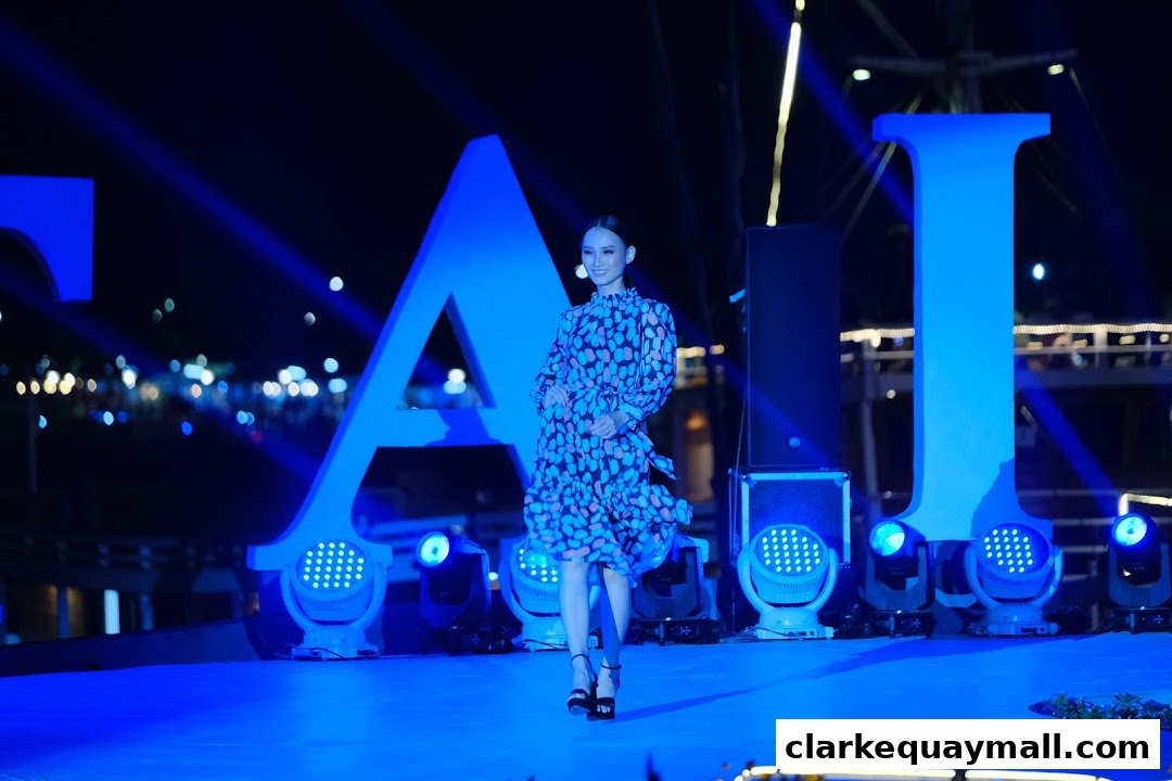 A woman in a patterned dress poses on a stage with large illuminated letters and spotlights.
