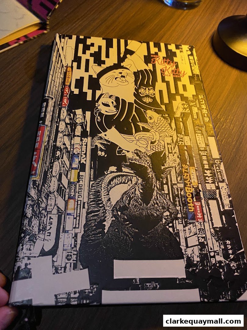 A book cover with a black and white design featuring cats, a monster, and Japanese cityscapes.