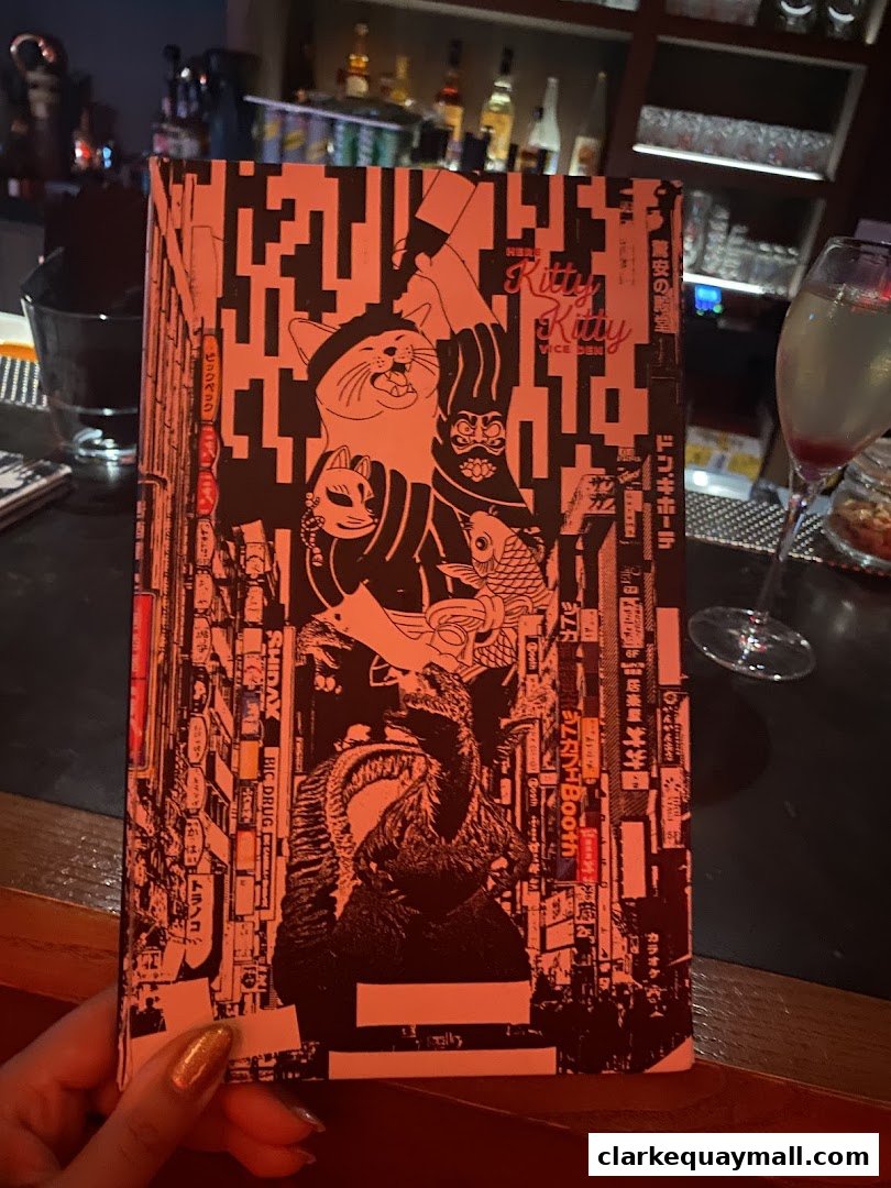 A person holds a menu with a stylized cat and Japanese text in a dimly lit cocktail lounge.