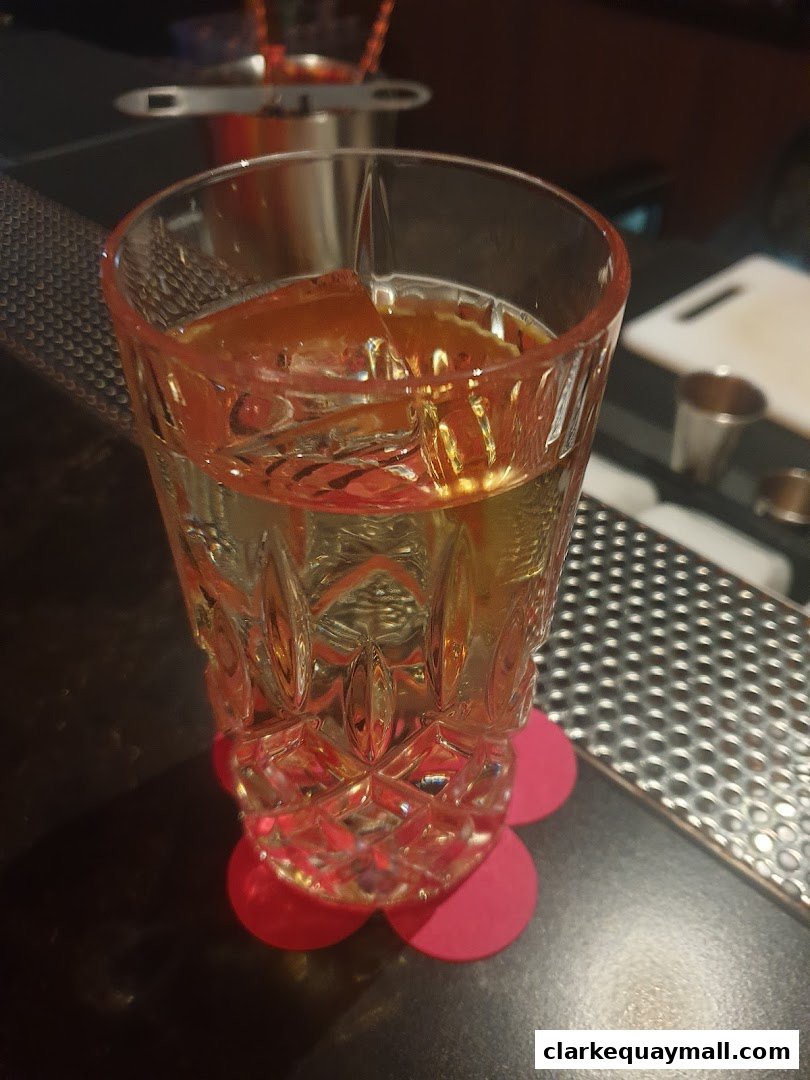 A close-up of a cocktail with ice and orange slices in a decorative glass on a bar.