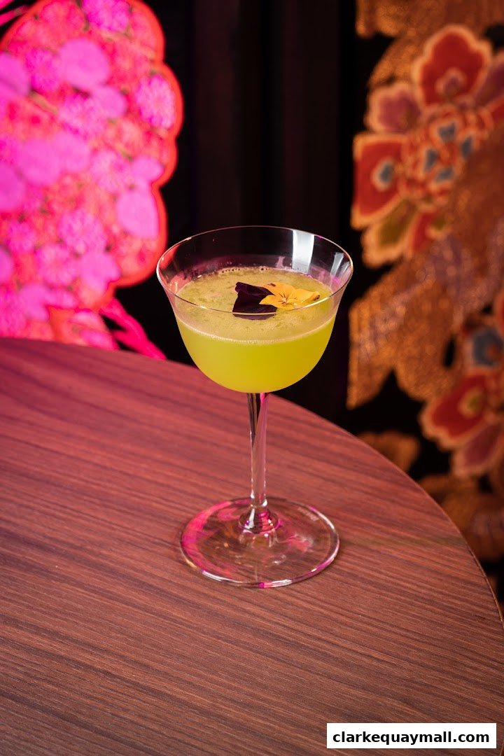 A vibrant green cocktail garnished with edible flowers sits on a wooden table.