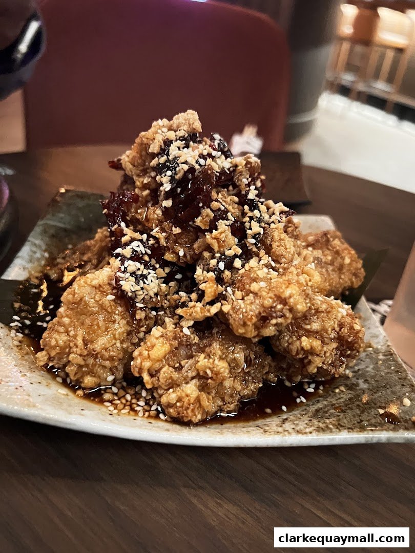 A plate of crispy fried chicken pieces drizzled with a dark sauce and topped with sesame seeds and nuts.
