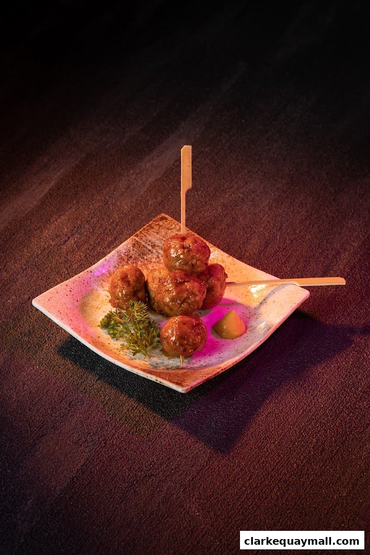 A plate of glazed meatballs on skewers with a side of mustard and garnish.