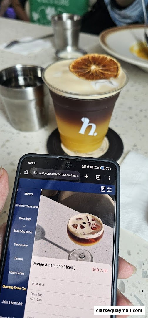 A person is holding a phone displaying a cafe's online menu with a coffee drink in the background.