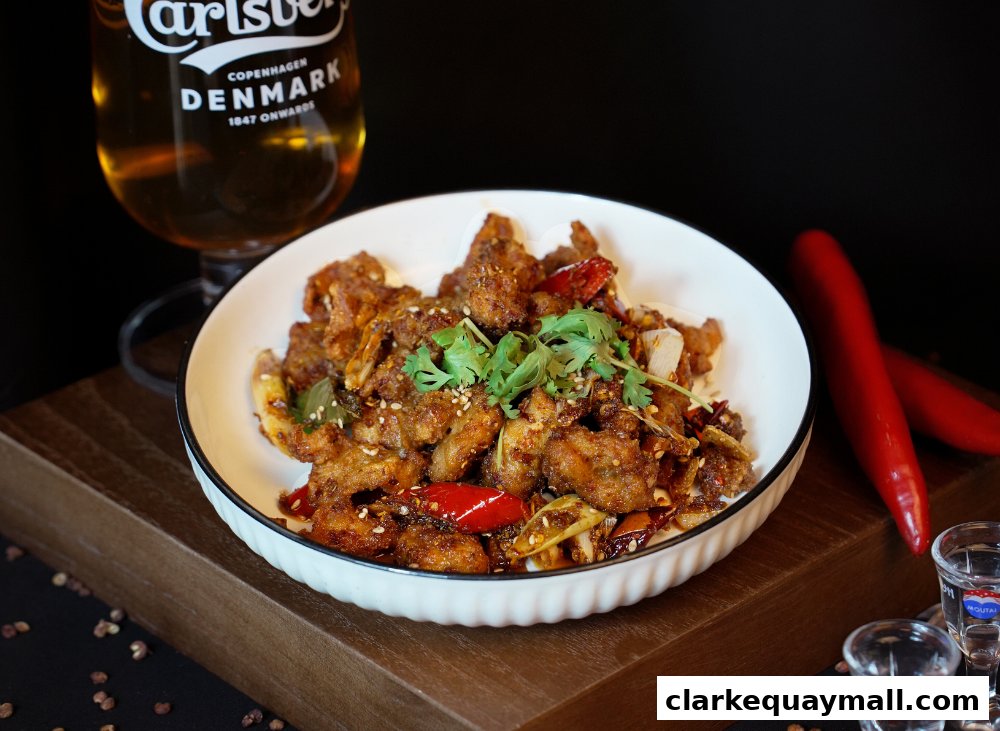 A plate of spicy fried chicken with chili peppers and cilantro, served with beer.