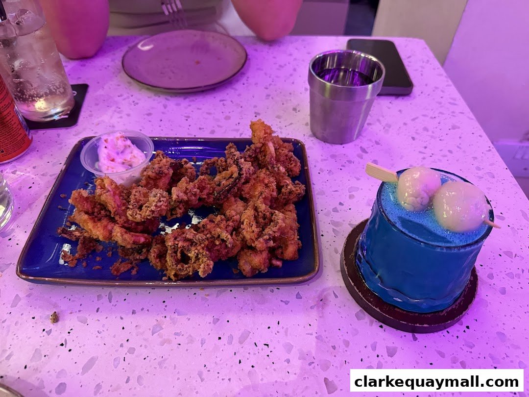 A plate of fried calamari and a blue cocktail with lychee on a table.
