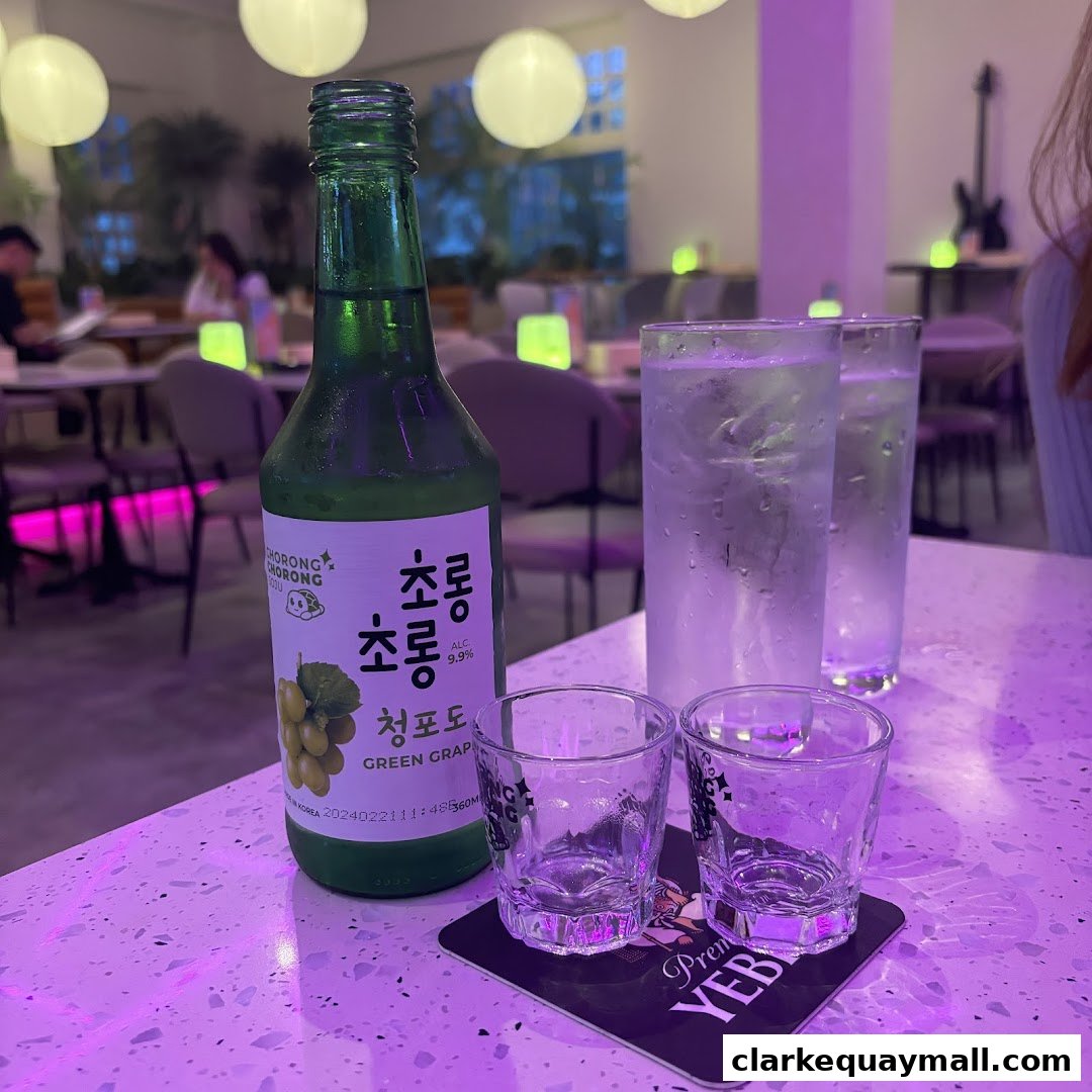 A bottle of green grape soju with two glasses and shot glasses on a table.