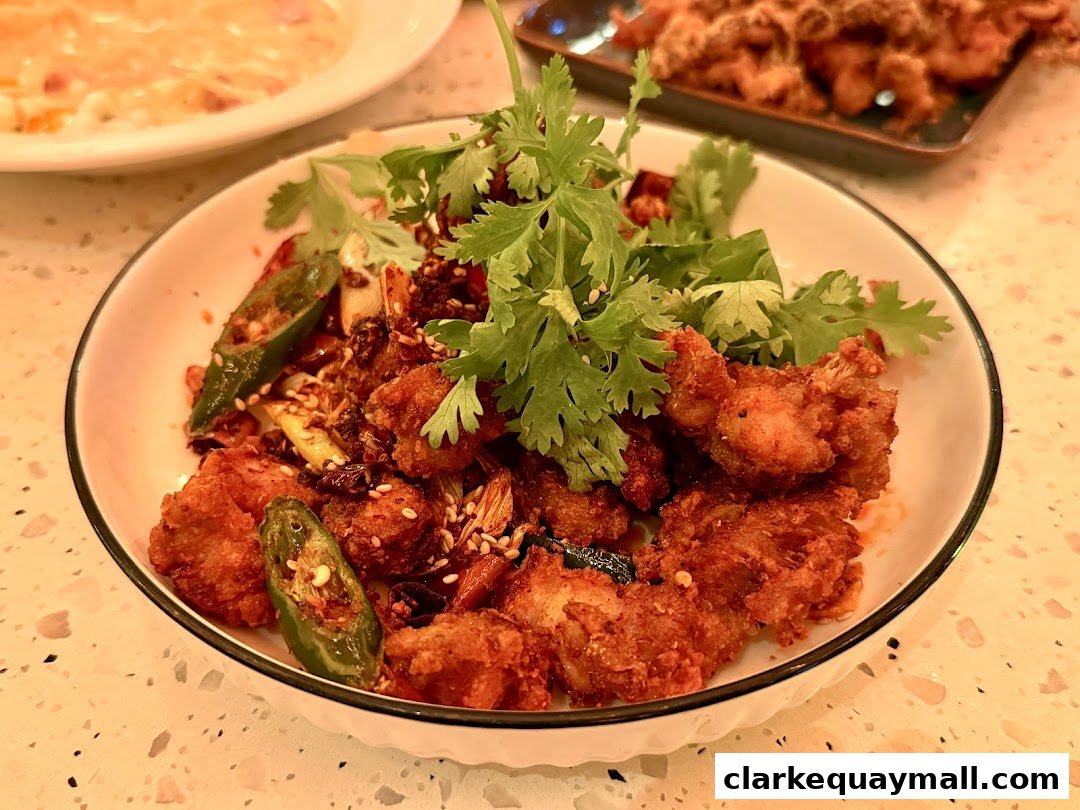 A close-up of a spicy fried chicken dish with cilantro and chili peppers.