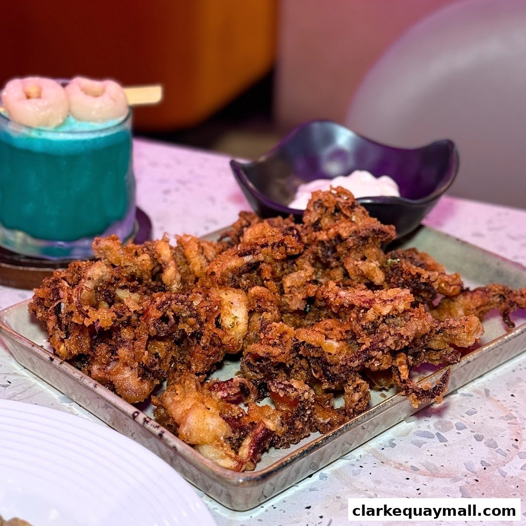 A plate of crispy fried calamari served with a dipping sauce and a blue cocktail.