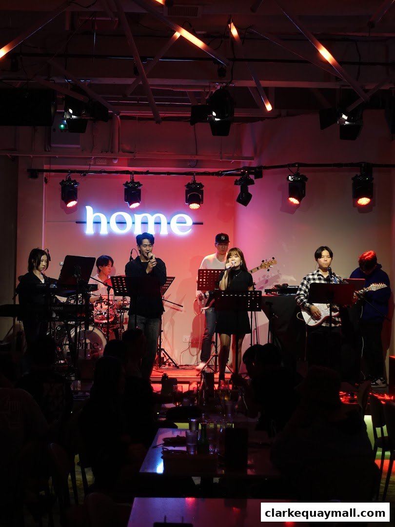 A live band performs on stage at Home Dusk Live House, with neon lights and audience in the foreground.