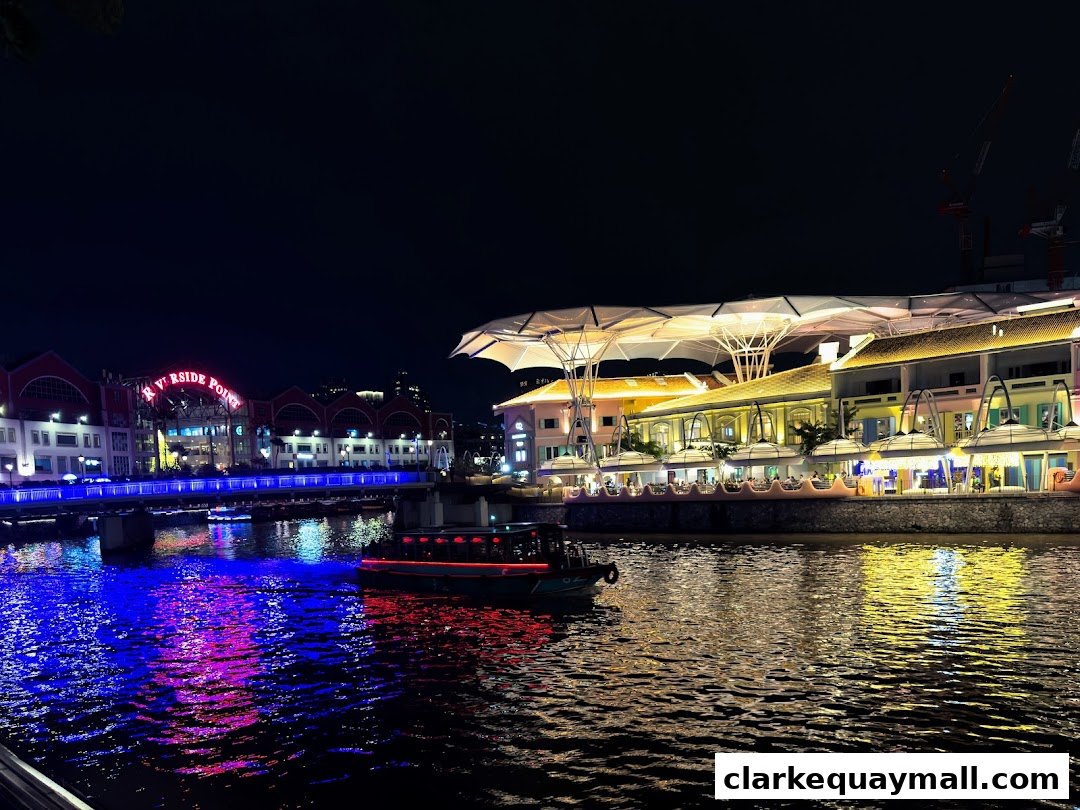 A scenic night view of Riverside Point with illuminated buildings and a boat on the water.