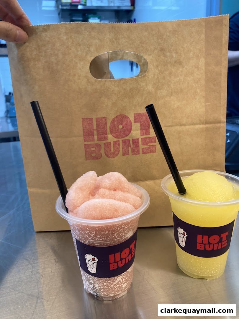 Two refreshing slushy drinks from Hot Buns with a branded paper bag in the background.