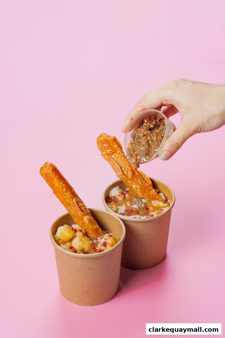 A hand is pouring sauce onto two cups of food with breadsticks.