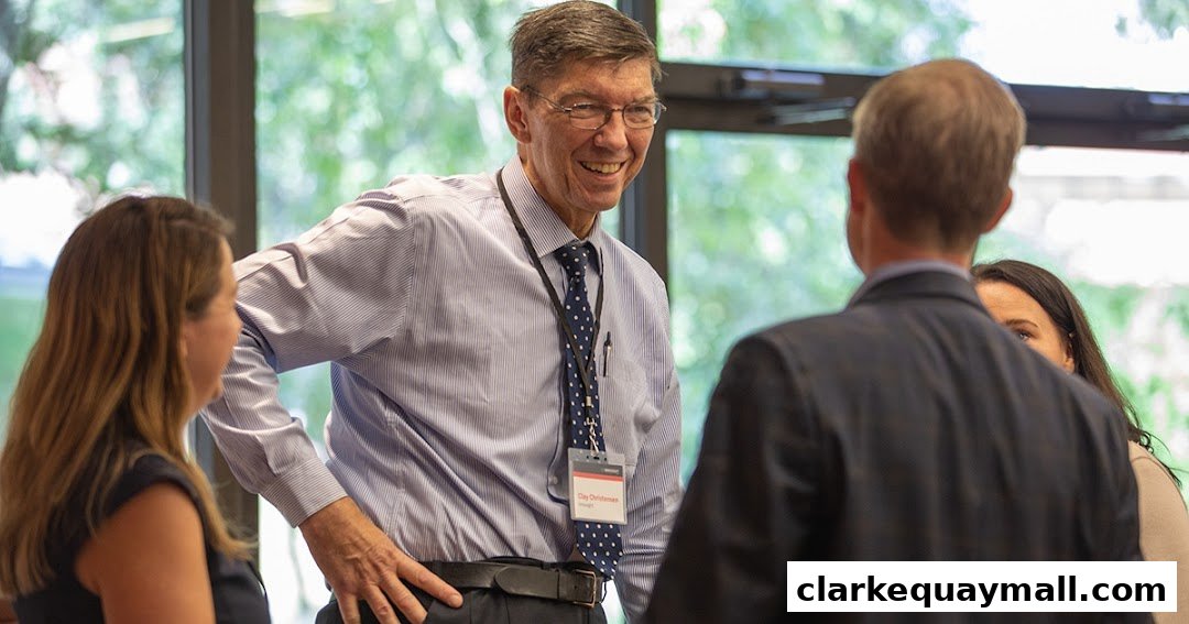A man in a striped shirt and tie smiles while talking to colleagues in a meeting.