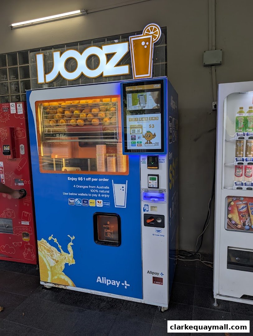 A blue and white vending machine dispensing fresh orange juice, with a sign for "iJooz".