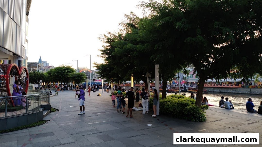 People enjoying a waterfront promenade with trees and buildings in the background.