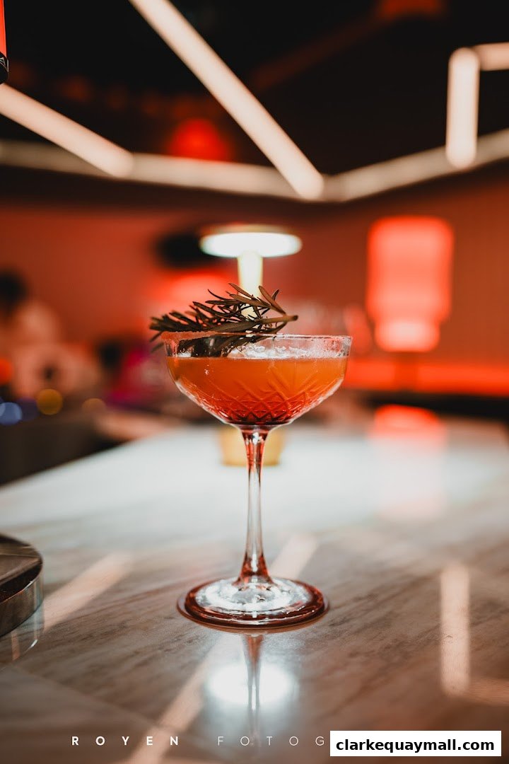 A close-up of a cocktail with rosemary garnish on a marble table.