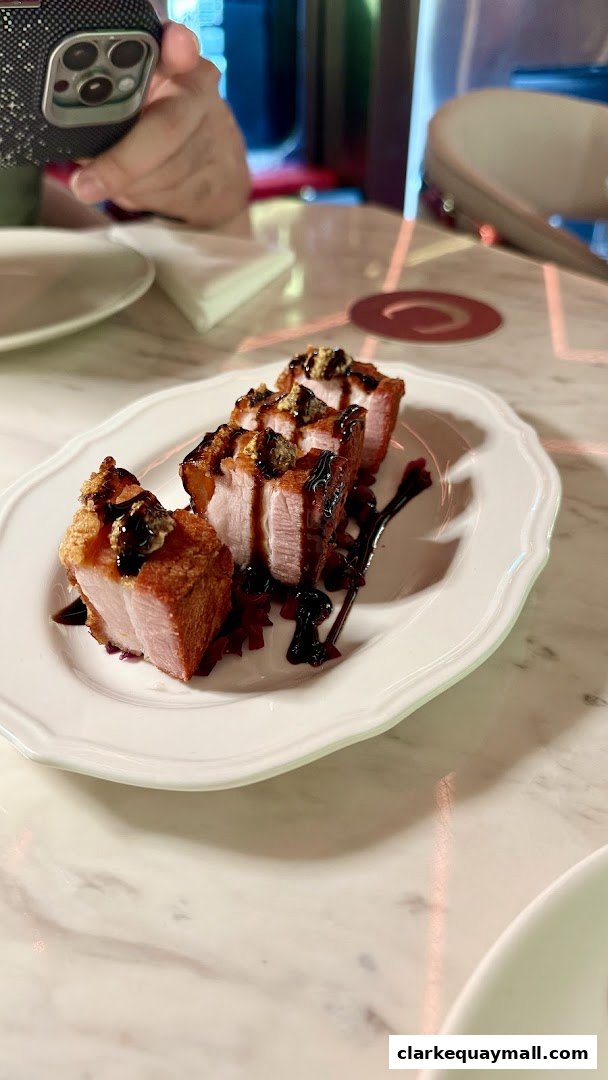 Crispy pork belly bites drizzled with sauce and topped with garnish on a white plate.