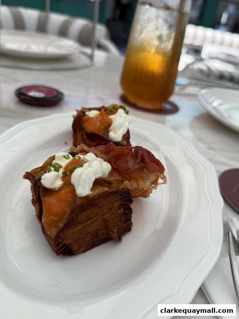 A close-up of two savory pastries topped with cream, salmon, and chives, served on a white plate with a drink.