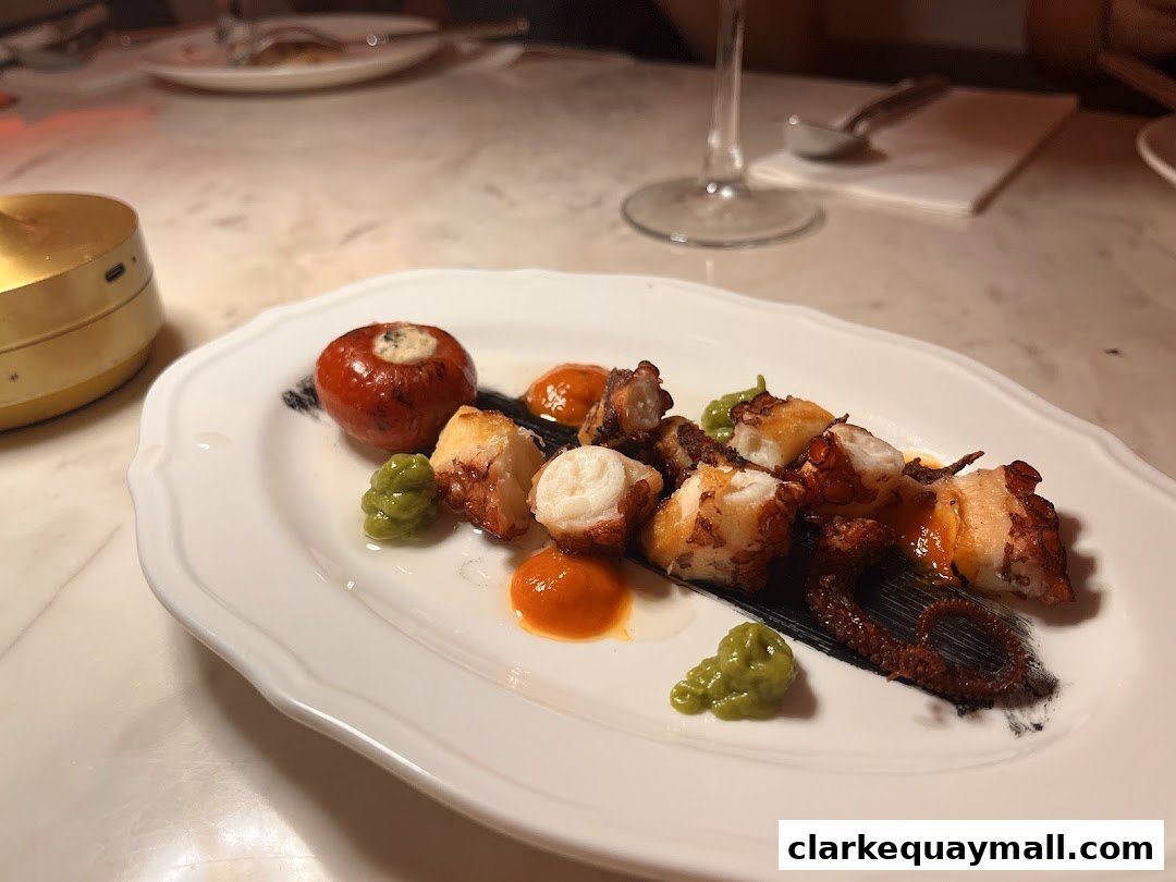 A plate of grilled octopus with a stuffed tomato and green puree.