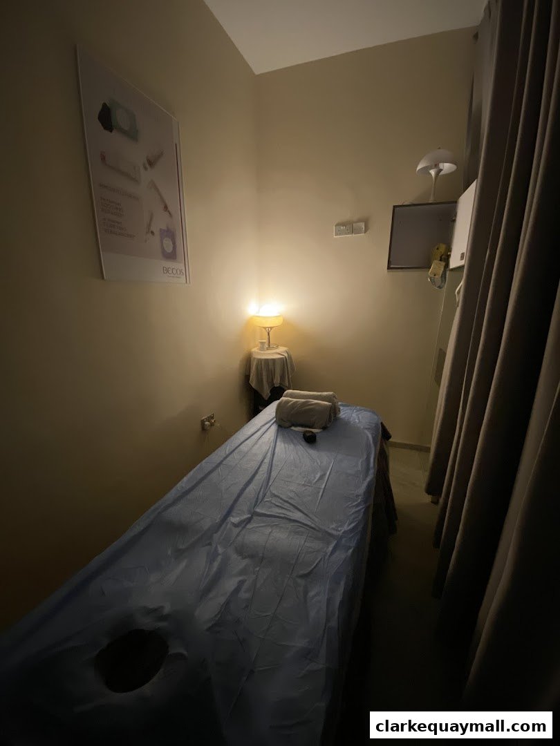 A dimly lit treatment room with a massage bed, towels, and a poster on the wall.