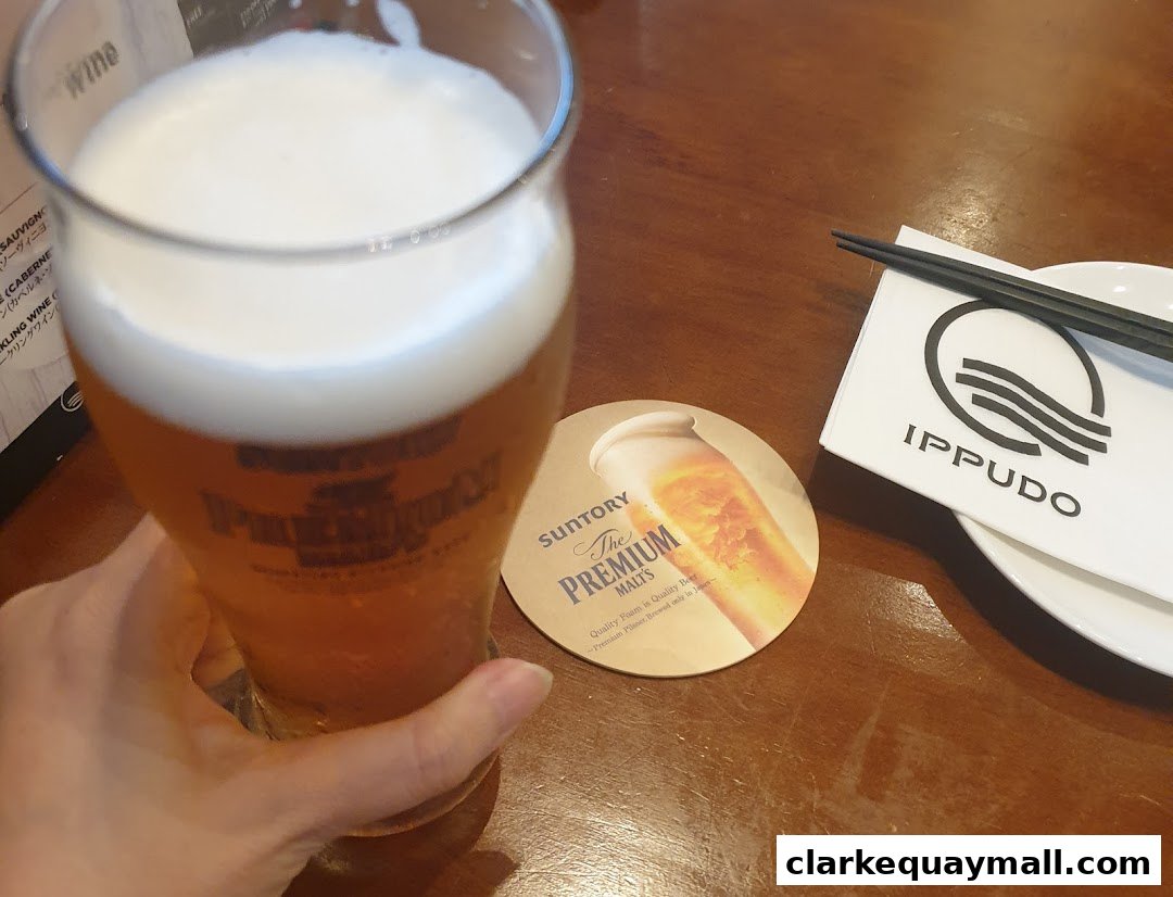 A hand holds a glass of beer next to a coaster and IPPUDO branded napkin.