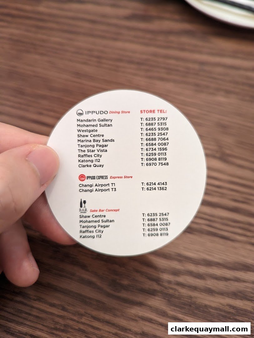 A hand holds a circular card listing IPPUDO store locations and phone numbers.