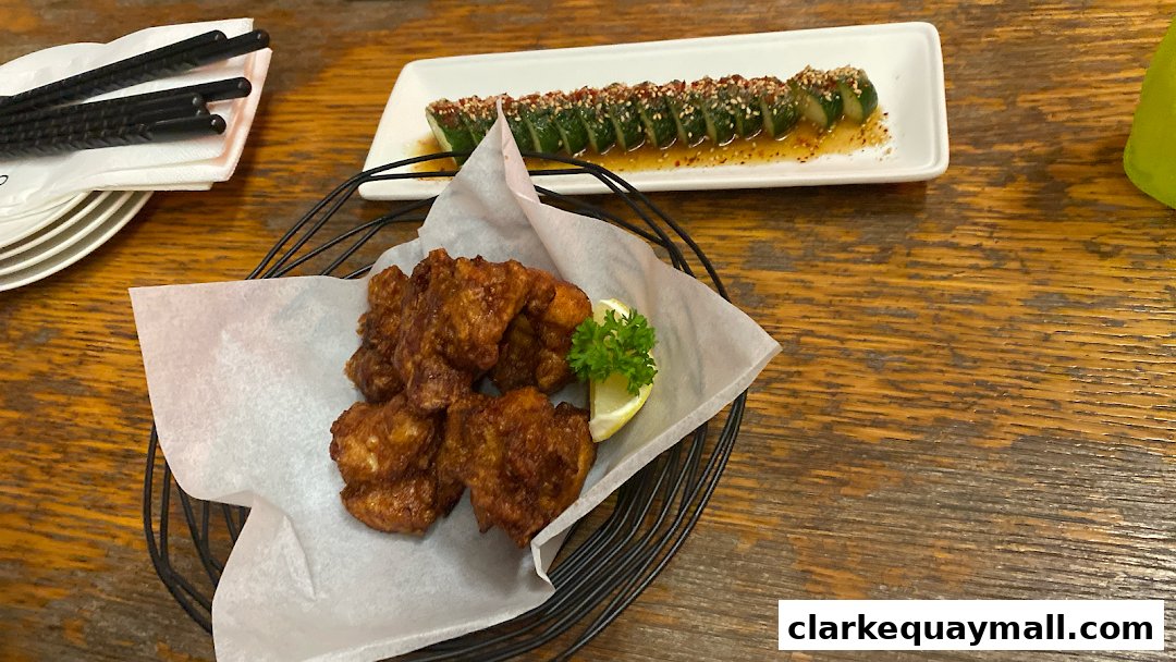 A basket of crispy fried chicken and sliced cucumbers with sesame seeds on a wooden table.