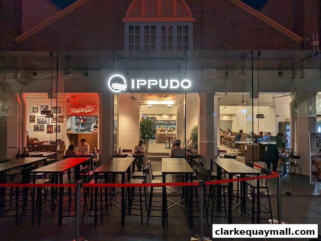 The exterior of Ippudo Clarke Quay restaurant at night, with tables and chairs visible inside.