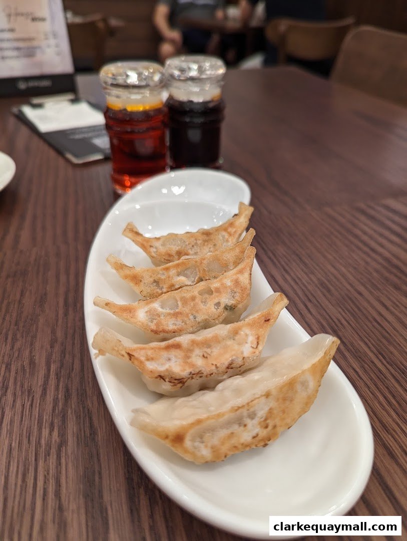 A plate of pan-fried dumplings served with dipping sauces on a wooden table.