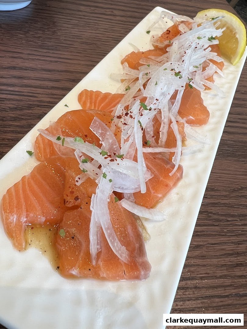 A plate of salmon sashimi with shredded daikon and a lemon wedge.